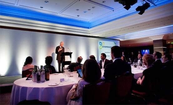 President Bill Clinton speaking from a lectern to guests seated at round tables at the charity gala dinner in London